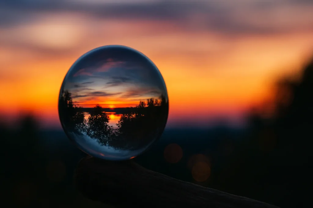 Cristal sobre tronco refletindo o pôr do sol, com céu laranja e azul, representando energia vibracional e sinais do universo (23:23).