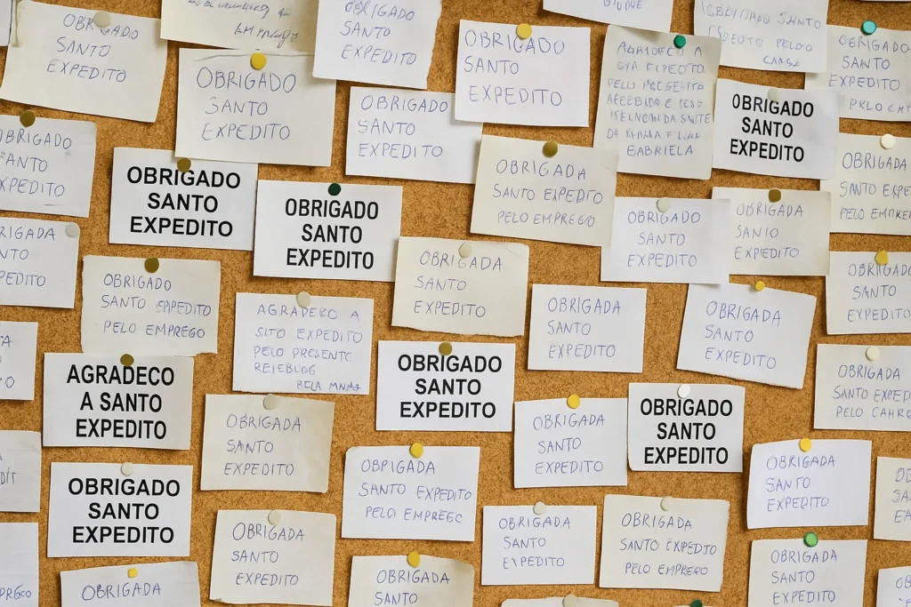Mural repleto de bilhetes escritos por devotos com mensagens de agradecimento a Santo Expedito por graças alcançadas em diferentes áreas da vida.